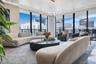 Floor-to-ceiling windows, sculptural LED chandelier, tray ceiling with recessed cove lighting, and stone flooring