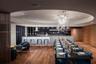 Circular recessed ceiling detail with a sculptural glass chandelier, wood-finish flooring, full-height wood-paneled walls, and a stone-topped island w