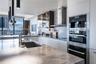 Contemporary kitchen featuring stone countertops, integrated stainless steel appliances, matte-finish flat-panel cabinetry, glass-front upper storage,