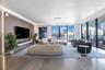 Living area featuring floor-to-ceiling windows, wood-paneled accent wall, recessed perimeter lighting, custom floating media console, and large-format