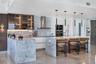 Kitchen featuring stone-clad islands and countertops, integrated stainless steel appliances, upper cabinetry with glass-front display panels, matte bl