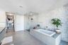 Bathroom featuring a deep-soaking drop-in tub with a stone-surround deck, a seamless glass-enclosed shower, stone mosaic wall tiling, large-format flo