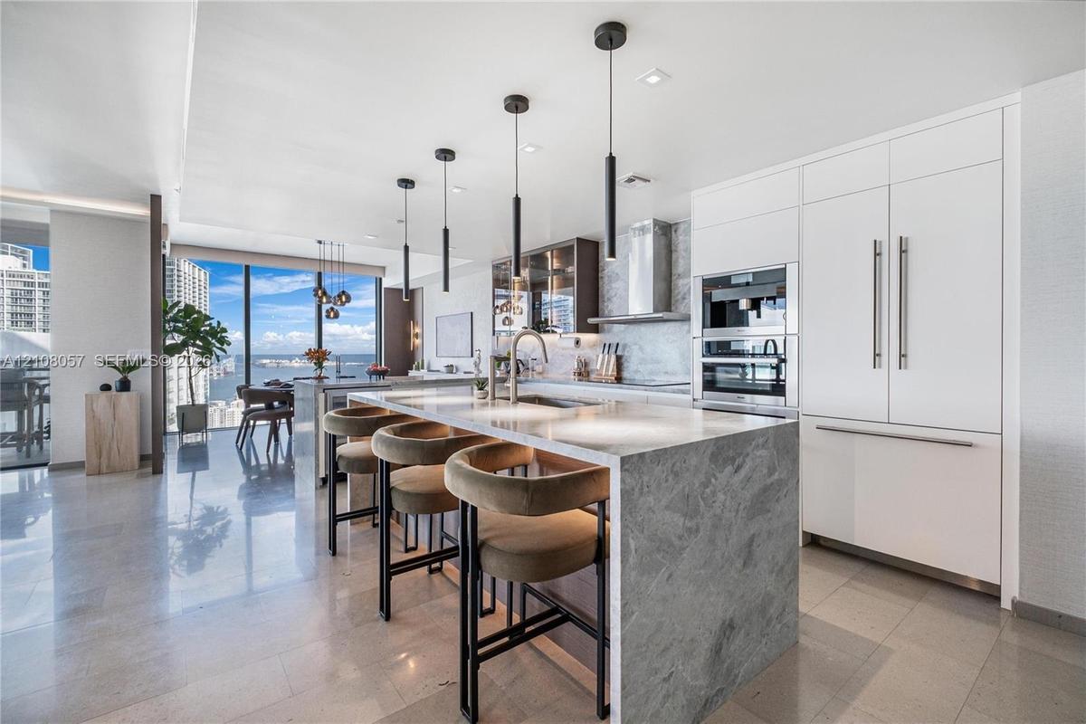Kitchen featuring a stone-topped waterfall island, built-in stainless steel appliances, floor-to-ceiling cabinetry, stone flooring, and contemporary p
