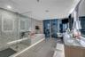 Bathroom featuring floor-to-ceiling windows, a glass-enclosed walk-in shower with stone tile wall, a soaking tub with stone surround, and a dual-sink 