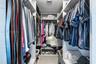 Custom reach-in closet featuring floor-to-ceiling white shelving units, integrated hanging rods, and neutral stone-finish flooring
