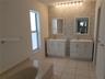 Dual white vanities with integrated sinks, penny-round tile backsplash, tiled flooring, built-in soaking tub, and matching rectangular wall mirrors