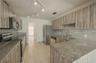 Kitchen featuring textured wood-finish cabinetry, stone countertops, stone backsplash, stainless steel appliances, and tile flooring