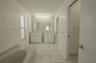 Dual white vanities, multi-colored stone-tiled accent wall, built-in soaking tub, large-format tile flooring, and multi-bulb integrated vanity lightin