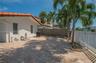 Rear exterior patio featuring a light-toned paver surface, white metal fencing, and mature palm trees