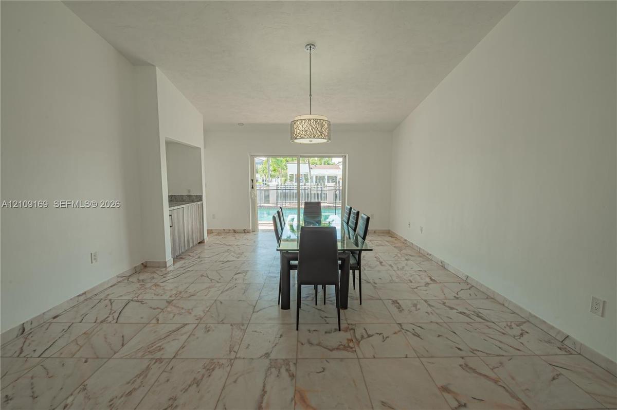 Vaulted ceilings, large-format tile flooring with veined detail, built-in wet bar, cylindrical pendant light fixture, and sliding glass doors opening 