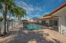 Outdoor area featuring a swimming pool, stone-paver patio, terracotta roof tiles, and palm trees