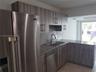 Kitchen featuring wood-grain cabinetry, stone countertops, stainless steel appliance suite, dual-basin stainless steel sink with high-arc faucet, and 
