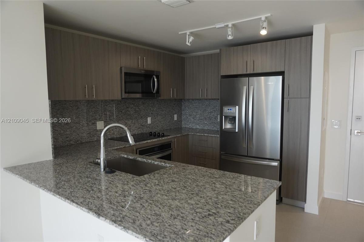 Kitchen featuring stone countertops, flat-panel cabinetry, stainless steel appliances, a single-basin undermount sink, and track lighting