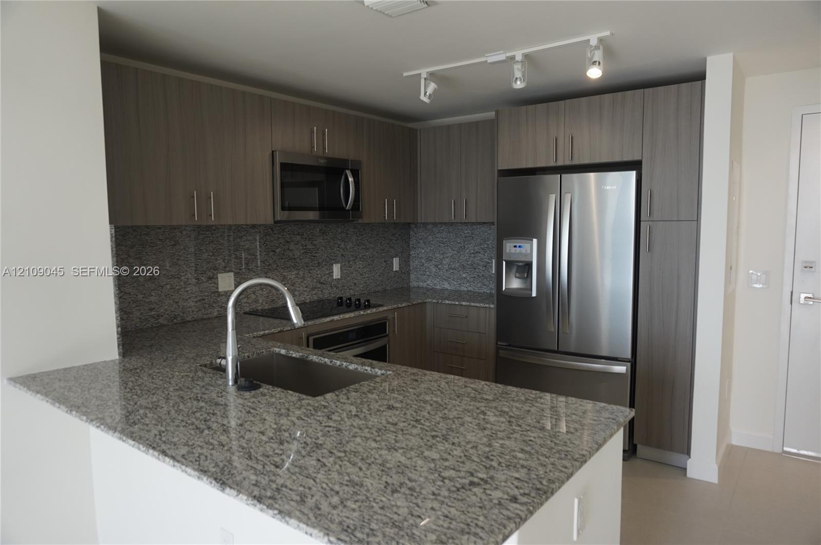 Kitchen featuring stone countertops, flat-panel cabinetry, stainless steel appliances, a single-basin undermount sink, and track lighting