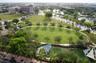 Expansive green space featuring mature trees, paved walking paths, curated landscaping, and shaded recreation structures