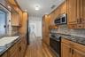 Galley kitchen featuring wood cabinetry with matte black hardware, stone-surface countertops, decorative tile backsplash, wood-finish flooring, and st