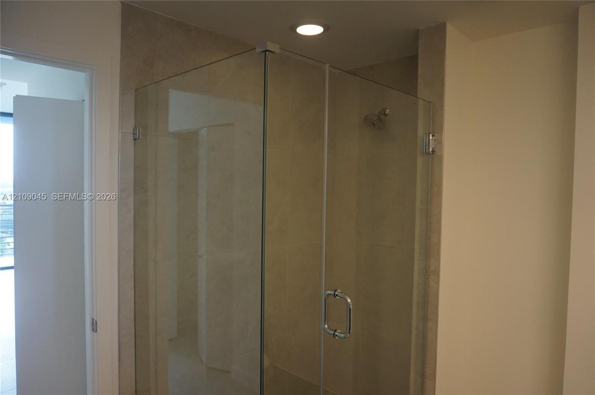 Shower enclosure with seamless glass panels, a polished metal handle, neutral-toned tiled surround, and a recessed ceiling light
