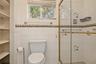 Bathroom featuring white wall tiling with decorative accent trim, glass-enclosed shower with gold-tone hardware, built-in recessed shelving, and a dou