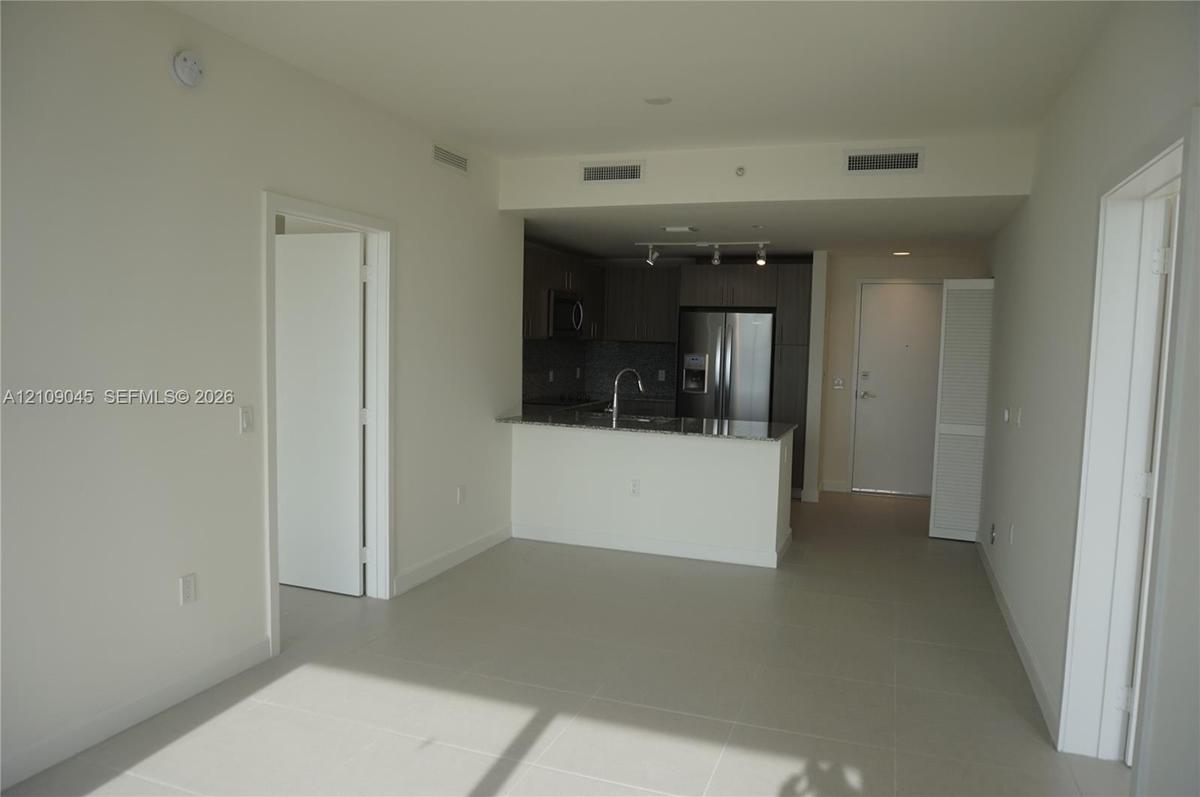 Open-concept kitchen featuring dark flat-panel cabinetry, stone countertops, stainless steel appliances, a gooseneck faucet, and large-format tile flo