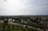 Elevated panoramic perspective featuring expansive green spaces, mature palm trees, multi-story commercial structures, and a distant urban horizon
