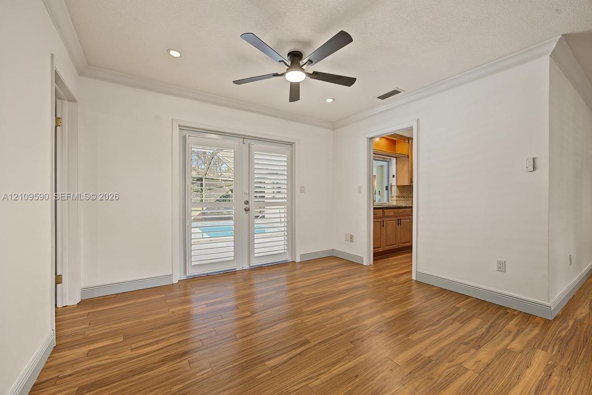 Room featuring wood-finish flooring, crown molding, ceiling-mounted light fixture with fan, and double glass doors with built-in shutters