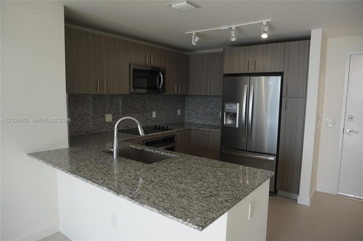 Kitchen featuring stone countertops, flat-panel cabinetry, stainless steel appliances, a breakfast bar, and track lighting