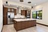 Kitchen featuring dark wood-finish cabinetry, a quartz-topped center island with integrated sink, stainless steel appliances, tiered glass globe penda