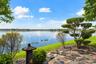 Waterfront property featuring a stone paver terrace, manicured lawn, tiered topiary landscaping, and a decorative stone lantern