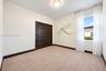 Neutral-toned carpeted room featuring dark-finished sliding closet doors, a flush-mount ceiling light, and a single window with curtain rod hardware