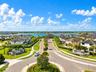 Aerial view of residential community featuring a paved roundabout, manicured landscaping, concrete sidewalks, multi-story residences, and a large lake