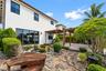 Stucco exterior featuring a wood-beam pergola, stone-paved patio, custom rock garden landscaping, and sliding glass doors