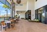 Covered outdoor patio featuring tile flooring, stone-accented support columns, expansive floor-to-ceiling glass panel walls, and a geometric pendant l