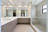 L-shaped vanity with wood-finish cabinetry, dual vessel sinks, quartz countertops, full-wall mirrors, and a glass-enclosed shower featuring stone floo