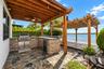 Outdoor kitchen featuring natural stone masonry, stainless steel built-in grill, and beverage refrigerator under a wood pergola, complemented by a sto