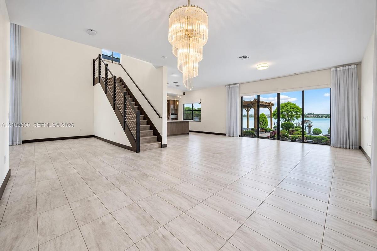 Open-concept living space featuring expansive floor-to-ceiling windows, a grand spiral chandelier, wood-finish tile flooring, and a staircase with a c