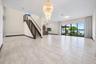 Open-concept living space featuring expansive floor-to-ceiling windows, a grand spiral chandelier, wood-finish tile flooring, and a staircase with a c