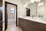 Double vanity featuring flat-panel cabinetry, light-toned stone countertops with integrated rectangular sinks, wall-to-wall mirror, and dual chrome fa