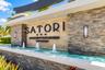 Community entrance featuring tiered stacked stone masonry, a multi-jet water feature, professional landscape lighting, and structural concrete framing