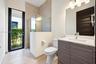 Bathroom featuring a floating vanity with a wood-finish cabinet and solid-surface countertop, a glass-enclosed walk-in shower with neutral tile surrou