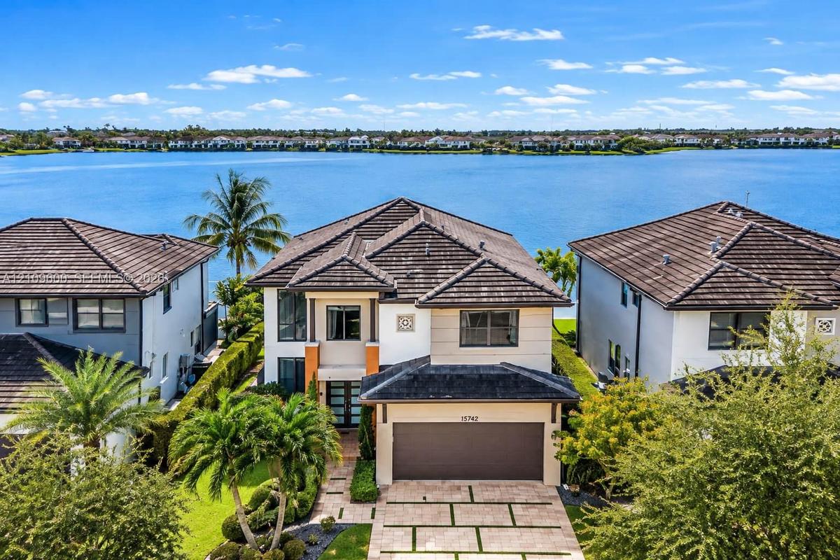 Two-story exterior featuring a hip roof, multi-pane glass entry door, paver driveway with integrated turf grid, and waterfront positioning