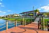 Private dock featuring composite decking, timber pilings with rope railing, and stone steps leading to an elevated patio with glass balustrade