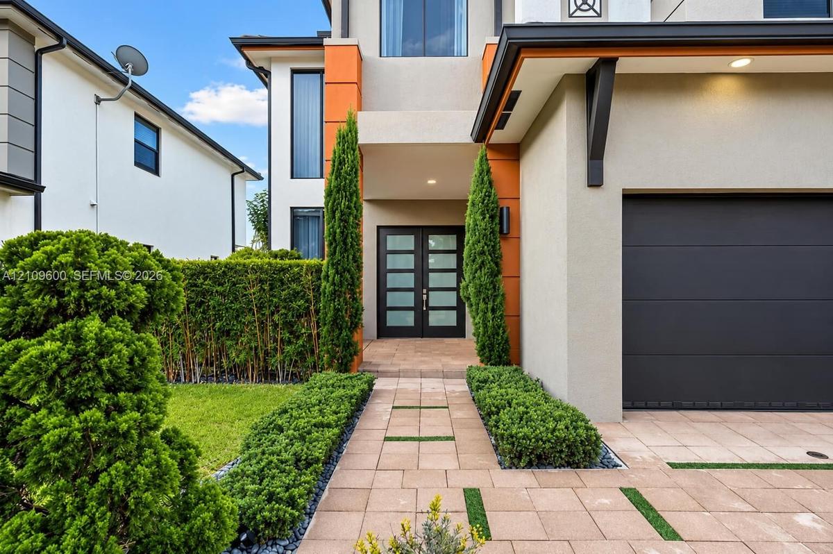 Contemporary two-story exterior featuring a paver walkway with turf inlay, double glass-paneled entry doors, and a multi-section garage door