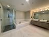 Bathroom featuring a glass-enclosed shower, soaking tub with stone-pattern surround, dual-sink floating vanity with wood-finish cabinetry, and large-f