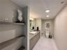 Built-in wood-finish shelving, vanity with integrated cabinetry, vessel sink, polished surface countertop, and large-format tile flooring