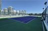 Rooftop tennis court featuring a blue and green multi-surface finish, perimeter chain-link fencing, and elevated stadium-style lighting