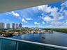 Covered balcony featuring a glass panel railing and panoramic waterway and urban skyline scenery