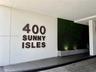 Covered entryway featuring dimensional signage, a green wall accent, concrete planter base, and stone paver driveway
