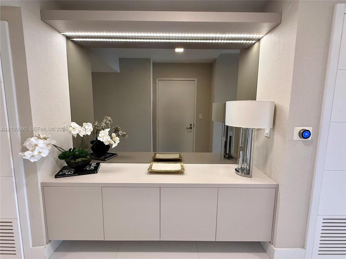 Built-in floating cabinetry featuring a solid surface countertop, expansive wall-to-wall mirror, and integrated LED accent lighting