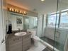 Bathroom featuring a wood-finish vanity with a drop-in sink, large wall-mounted mirror, walk-in shower with stone-style surround and glass enclosure, 