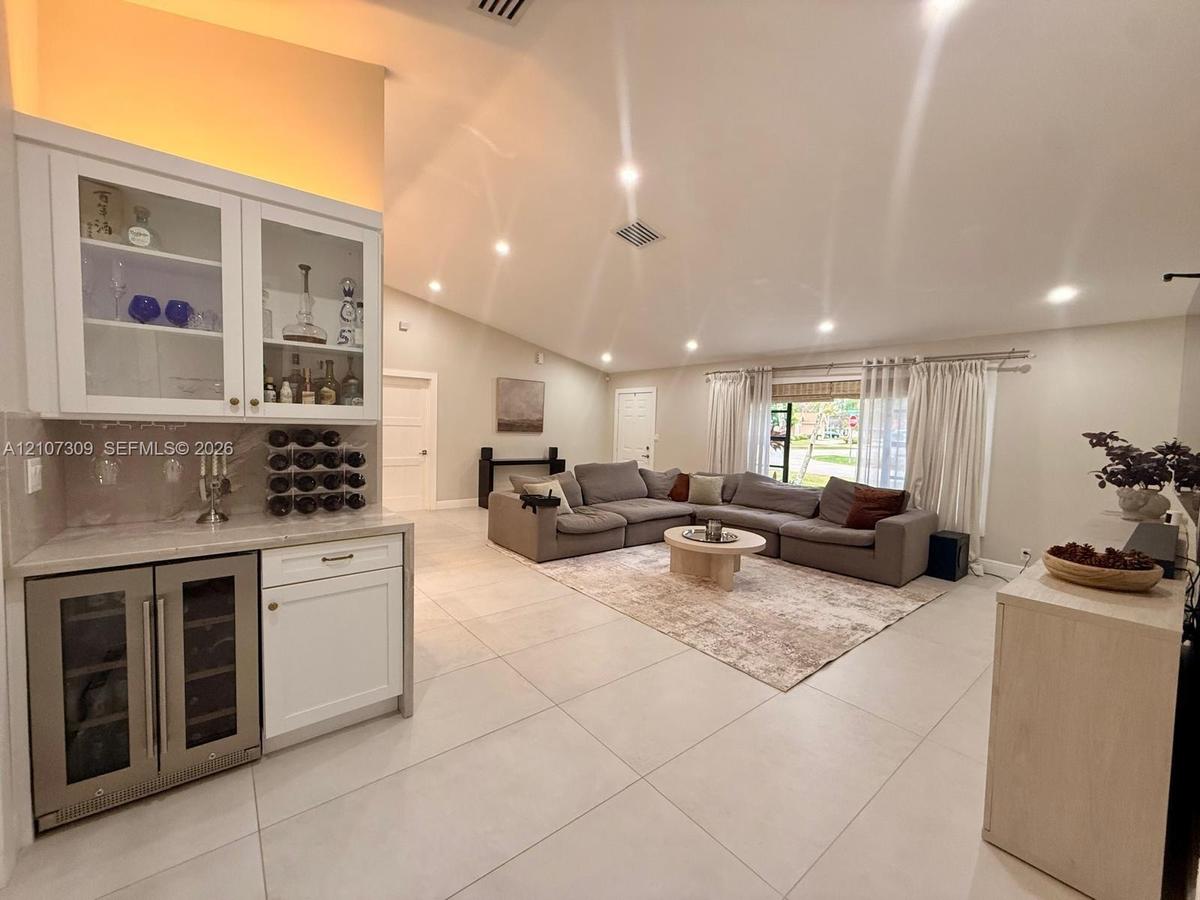 Built-in wet bar featuring white cabinetry, glass-front upper storage, a stone countertop, and an under-counter beverage refrigerator, set within an o
